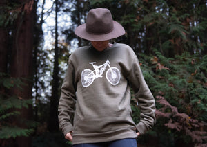 A young woman is wearing moss green pullover with a mountain bike design on it.