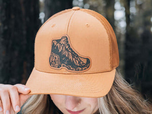 Hiking Boot, Trucker Hat worn by a woman in outdoor setting, designed in Canada, featuring Canadian artist illustration.