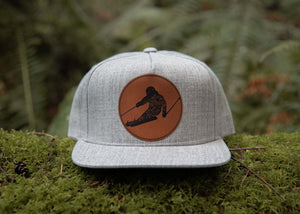 Skier Flat, Bill Hat with durable faux leather patch on a flat bill trucker design in a natural outdoor setting.