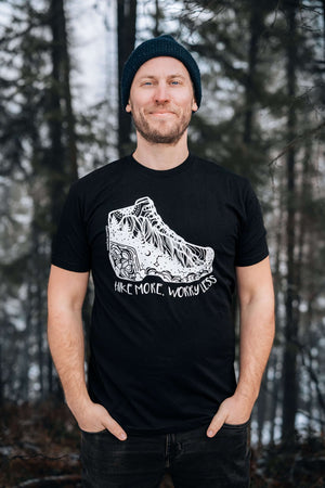 Man wearing Hike More, Worry Less; Unisex T-shirt, Responsibly Made in a forest setting.