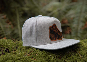 Hiking Boot, Flat Bill Hat on moss with eco-friendly design by a Canadian artist, perfect for outdoor adventures.