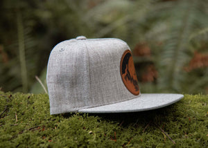 Moon and Climber Flat Bill Hat on mossy ground, perfect outdoor hat designed by a Canadian artist.