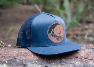 Moon and Climber Flat Bill Hat on a log, featuring a faux leather patch and a stylish design for outdoor adventures.