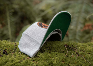 Moon and Climber Flat Bill Hat resting on moss in a forest, showcasing its faux leather patch and flat bill design.