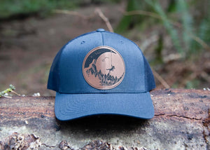Moon and Climber, Trucker Hat on a log, featuring a faux leather patch, perfect outdoor hat for women.
