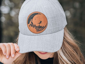 Moon and Climber, Trucker Hat worn by a woman outdoors, featuring a faux leather patch and adjustable snapback.