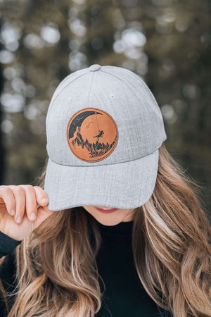 Moon and Climber Trucker Hat worn by a woman outdoors, featuring a faux leather patch and adjustable snapback.