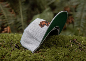 Mountain Bear Flat Bill Hat on moss, featuring faux leather patch, ideal for outdoor adventures.