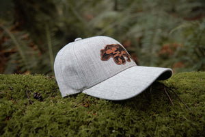 Mountain Bear Trucker Hat on mossy ground, showcasing the durable faux leather patch, designed for outdoor adventures.