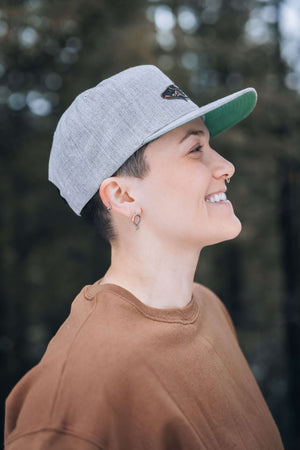 A woman showcasing the Salmon, Flat Bill Hat with a faux leather patch, perfect for outdoor adventures.