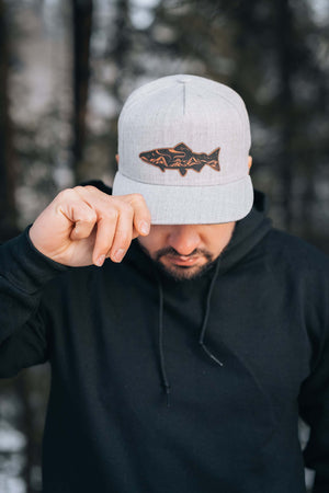 Salmon, Flat Bill Hat worn by a man, showcasing salmon design and durable faux leather patch in outdoor setting.