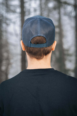 Back view of a man wearing a Sea to Sky flat bill hat in a forest setting, showcasing its adjustable snapback design.