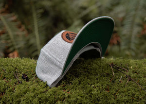Sea to Sky flat bill hat on green moss with faux leather patch, perfect for outdoor adventures and everyday wear.