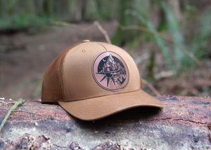 Sea to Sky Trucker Hat on a log in a forest, designed in Canada by a Canadian artist for outdoor adventures.