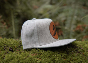 Skier Flat, Bill Hat resting on moss in a forest, featuring a faux leather patch and a natural background.