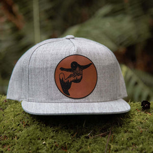 Snowboarder, Flat Bill Hat resting on moss, featuring a durable faux leather patch and adjustable snapback design.