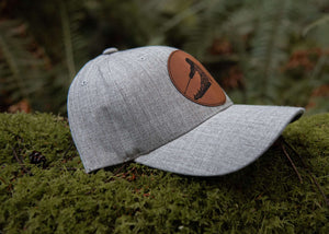 Skier, Trucker Hat resting on moss, featuring faux leather patch and designed for outdoor adventures.