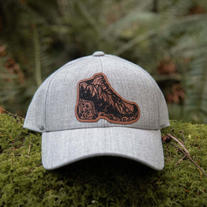 Hiking Boot, Trucker Hat with durable faux leather patch on a mossy forest floor.