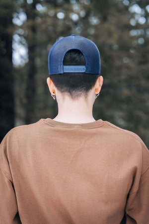 Skier, Trucker Hat worn by a young person in outdoor setting, showcasing the adjustable snapback design.
