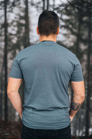 Back view of a man wearing a Salmon, Unisex T-shirt, Responsibly Made in a forest setting.