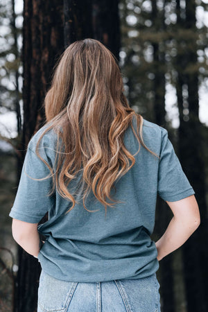 Salmon, Unisex T-shirt, Responsibly Made, showcasing the back view of a wearer in a forest setting.