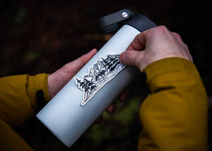 Bear and Mountain Sticker being applied to a water bottle, featuring a black and white original illustration of mountains.