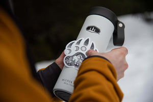 Person applying a Bear Claw Sticker to a gray thermos outdoors, showcasing the black and white vinyl design.