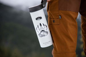 Bear Claw Sticker on a white travel mug held by a person in outdoor gear, showcasing an original black and white illustration.