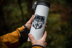 Bear Head Sticker on a travel tumbler in a forest setting, perfect outdoor sticker by Canadian artist.