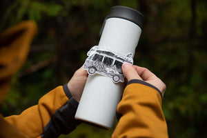 Person applying a Camper Van Sticker on a travel mug in an outdoor setting, showcasing a black and white original illustration.
