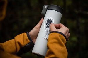 Person adding a Climbing Carabin Sticker to a white tumbler, showcasing an outdoor-themed design.
