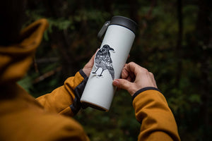 Person holding a travel mug featuring a Crow Sticker, a black and white outdoor vinyl sticker.