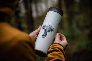 Deer Sticker on a travel mug held in forested setting, showcasing original black and white illustration by Canadian artist.