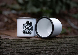 Dog Paw Enamel Mug on a log, featuring an original illustration by a Canadian artist for outdoor adventures.