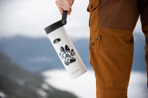 Dog Paw Sticker on a white tumbler held by a person wearing brown outdoor pants in a mountain landscape.