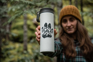 Dog Paw Sticker on a stainless steel tumbler held in a forest, showcasing a black and white original illustration.