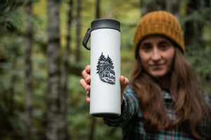 Forest Heart Sticker on a white travel mug held by a woman in a forest, showcasing outdoor adventure aesthetics.