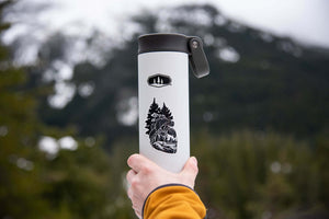Forest Heart Sticker on a stainless steel tumbler held outdoors against a mountainous backdrop.
