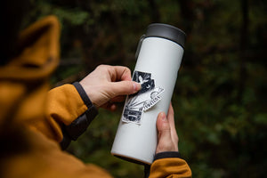 Person applying Manitoba Sticker on a white tumbler in an outdoor setting, showcasing outdoor sticker design.