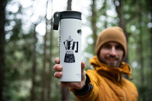 Moka Pot Coffee Sticker on a travel mug held by a person in a forest setting, showcasing original black and white illustration.