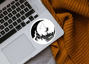 Moon and Climber Sticker on a laptop with a cozy blanket, featuring a black and white original illustration.