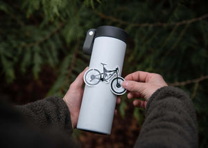 Person applying a Mountain Bike Sticker to a stainless steel tumbler in a natural setting.