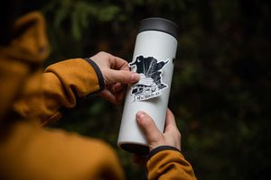 New Brunswick Sticker applied to a travel mug, showcasing its glossy vinyl finish and original black and white illustration.