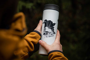 Person holding a travel mug featuring a black and white New Brunswick Sticker, showcasing original illustration made in Canada.