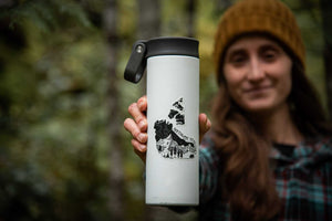 Northwest Territories Sticker on a travel mug held by a woman in a forest, showcasing a black and white outdoor sticker design.