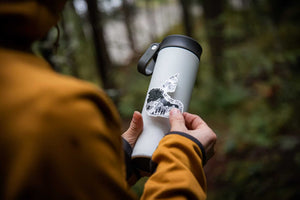 Person holding a travel mug with a Northwest Territories Sticker, featuring an original black and white illustration.