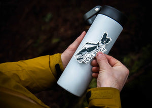 Person applying a Nova Scotia Sticker to a gray water bottle, showcasing a black and white original illustration.