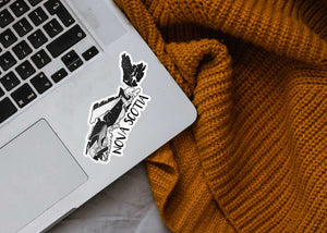 Nova Scotia Sticker on a laptop with a cozy knitted blanket, showcasing a black and white original illustration.