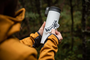 Person applying a Prince Edward Island Sticker to a water bottle outdoors, showcasing a black and white original illustration.