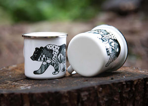Roaming Bear Enamel Mug displayed outdoors on a wooden surface, showcasing original illustration by a Canadian artist.